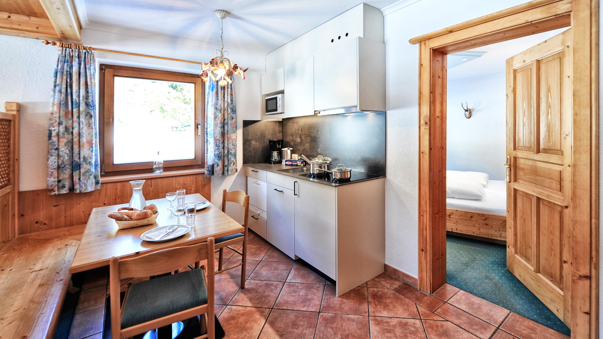 Helle Ferienwohnung mit moderner Küchenzeile, Esstisch und Blick ins Schlafzimmer mit Holzdetails im Apart Gabriele, St. Anton.