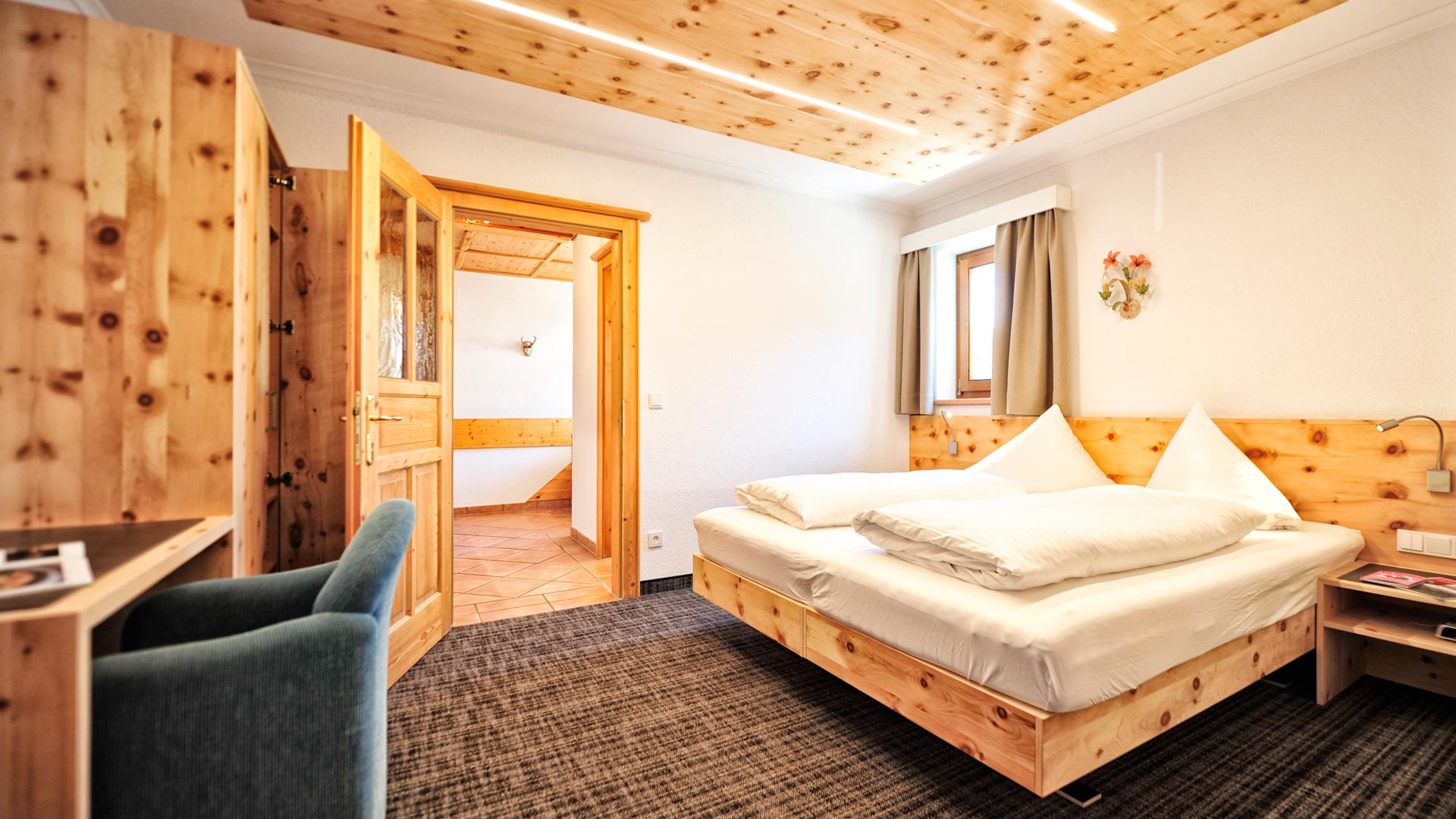 Helles Schlafzimmer mit Holzbett, modernem Lichtdesign an der Decke, Fenster, Schreibtisch und gemütlicher Einrichtung.