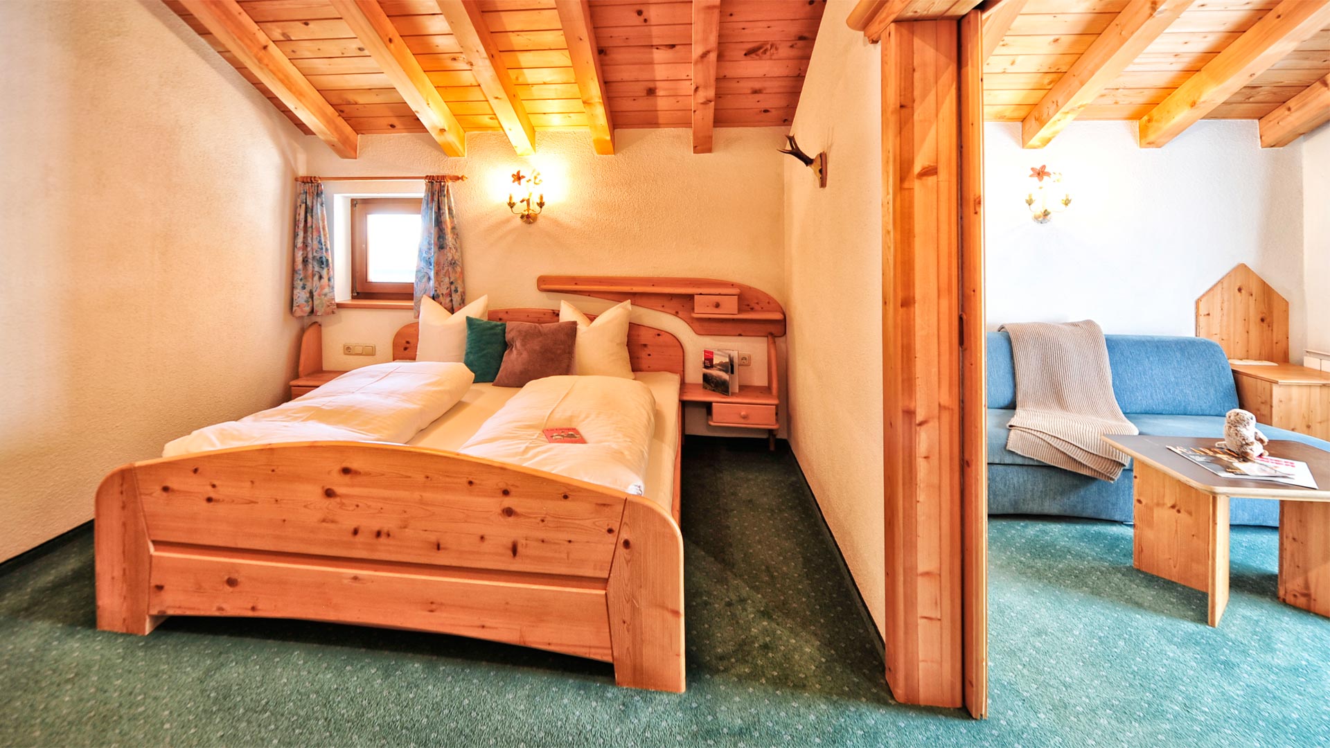 Gemütliches Schlafzimmer mit Holzbett und angrenzendem Wohnbereich mit Sofa unter einer Dachschräge im Landhausstil.